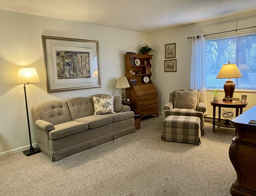 A living room with a grey sofa, a wooden cabinet, a chair, a table, and a lamp.