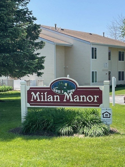 A sign for Milan Manor in front of a building.
