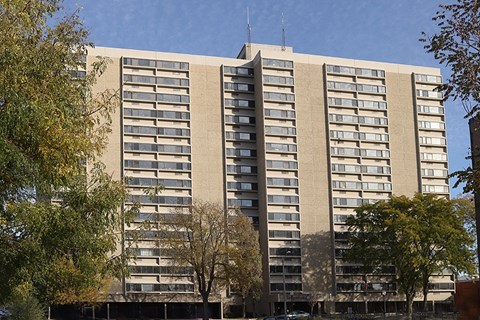 A large beige building with a flat roof and a tall antenna on top.