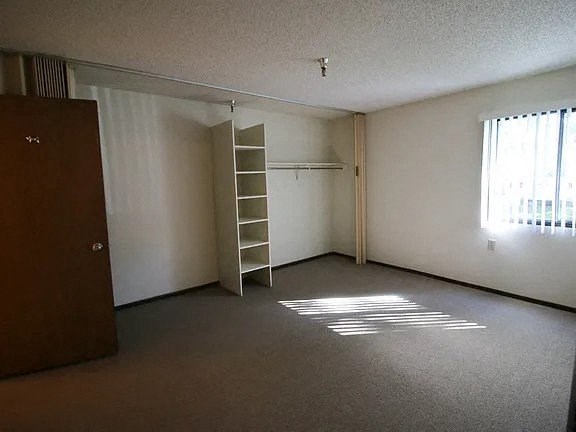 A room with a brown wardrobe and a white shelving unit.