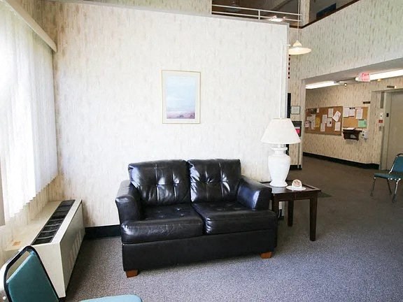 A black leather couch sits in a room with a white wall and a framed picture hanging above it.