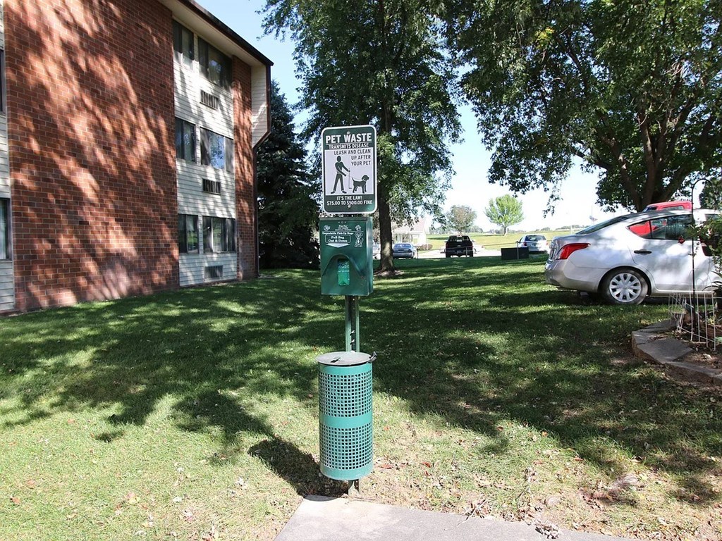A green trash can is in front of a sign that says "Pet Waste".