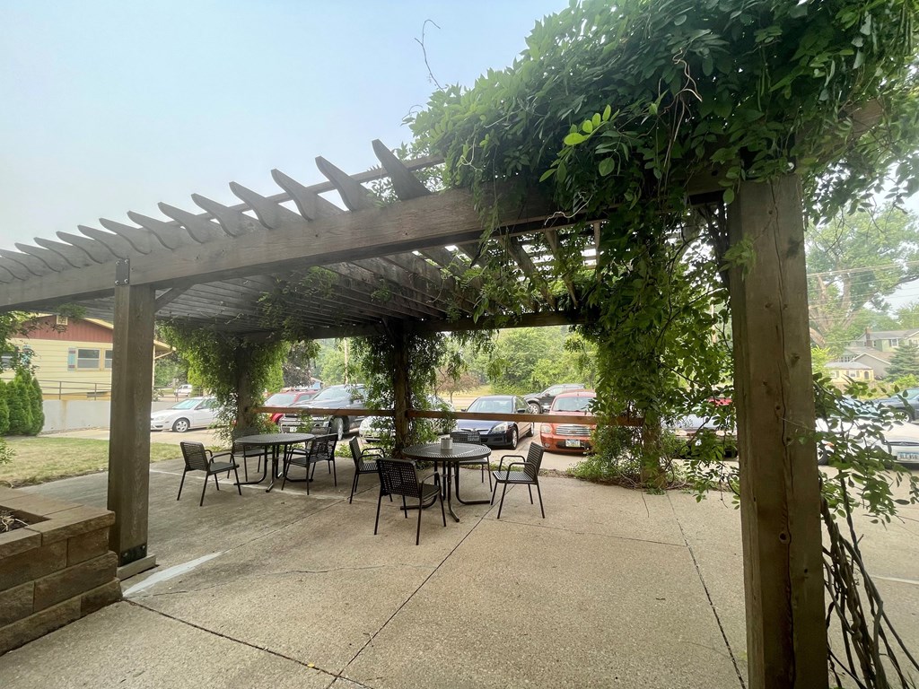 A wooden pergola with green vines growing on it is situated over a patio table.