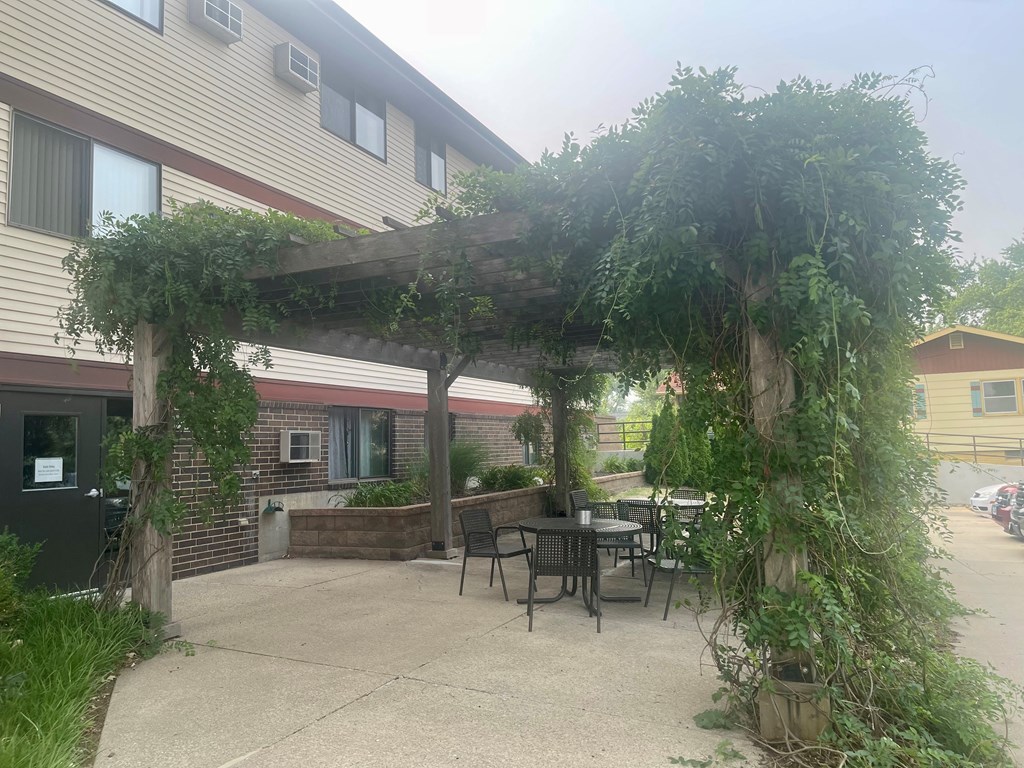 A patio with a table and chairs under a vine covered pergola.