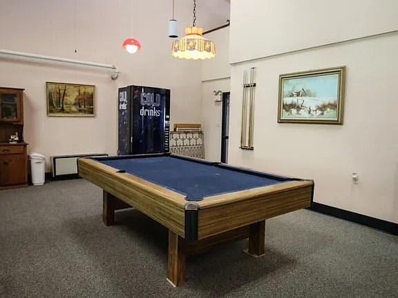A pool table in a room with a cabinet and a painting on the wall.
