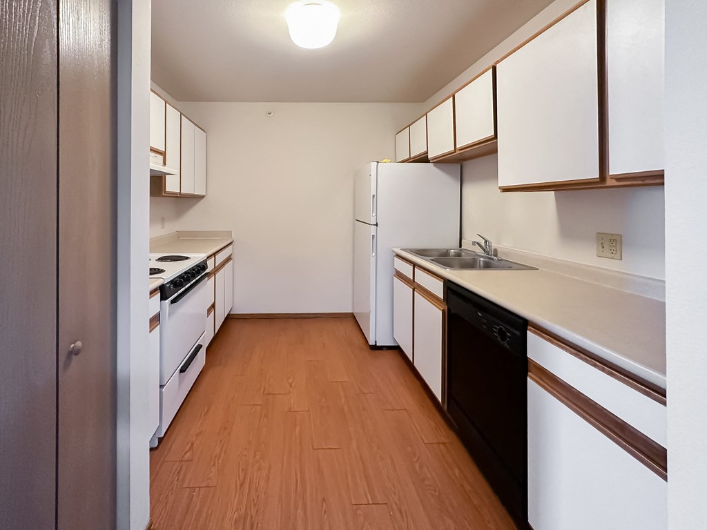 an empty kitchen with white appliances and wood flooring