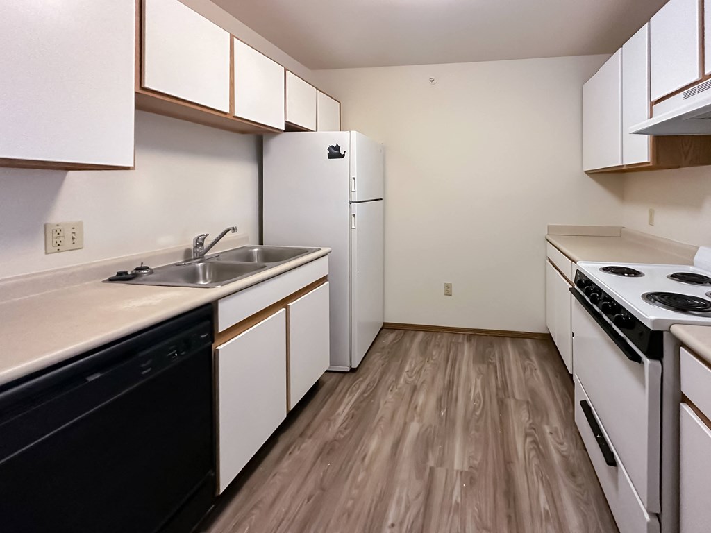 an empty kitchen with white cabinets and appliances and wood flooring