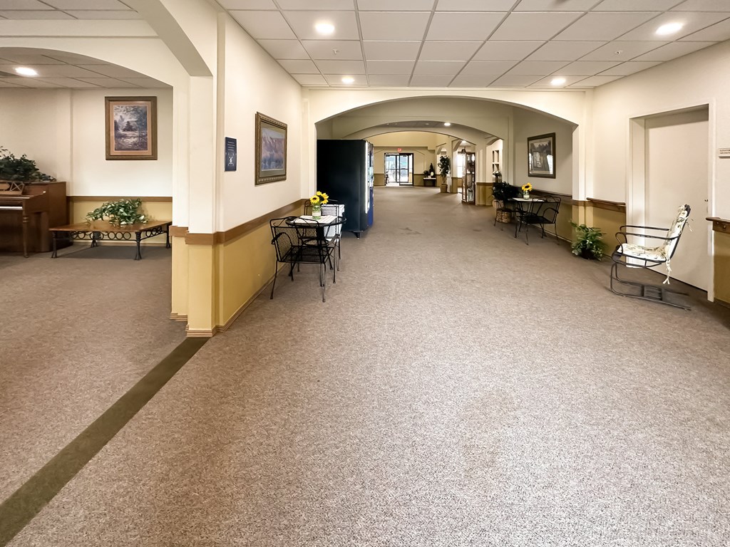 a hallway with tables and chairs in a building with a carpeted floor