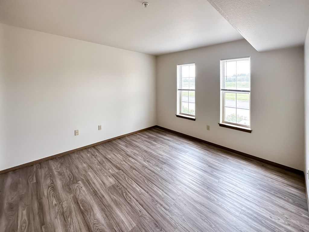 the living room of an empty house with wood flooring and two windows