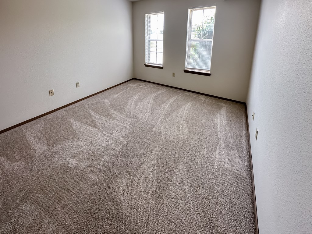 an empty room with carpet and two windows