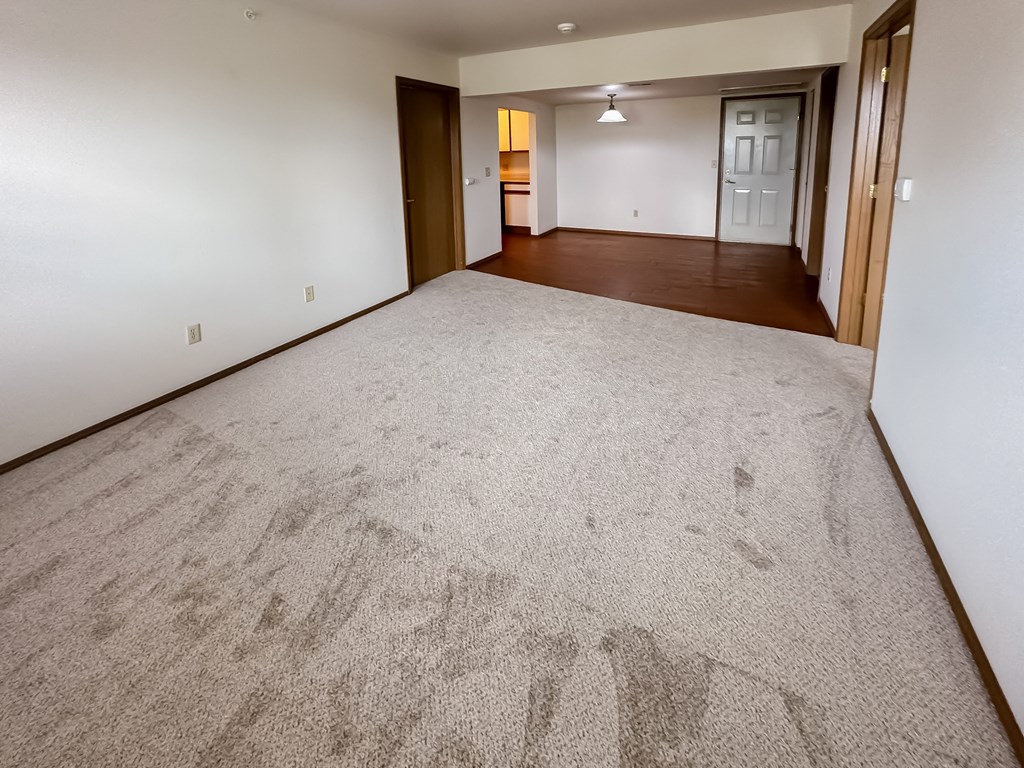 the living room and dining room of an empty home with carpeting and a door