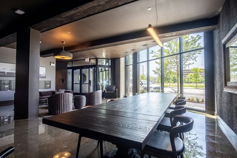 A long wooden table is surrounded by chairs in a room with a lot of windows.