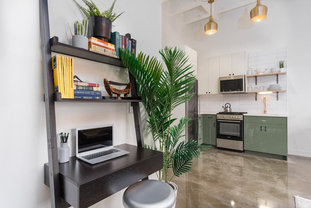 a living area with a desk with a laptop and a kitchen