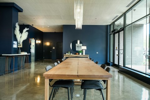 A long wooden table is surrounded by black chairs in a room with a white ceiling light.