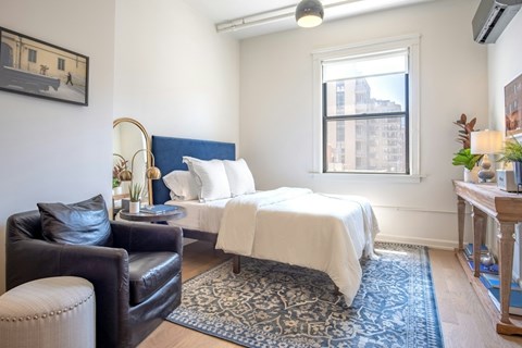 A bedroom with a bed, chair, and a window.