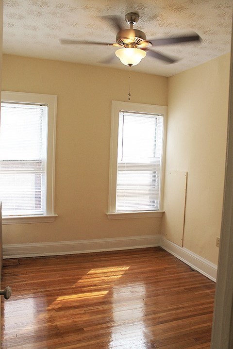 an empty room with a ceiling fan and two windows