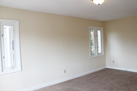 A room with a carpeted floor and two windows.