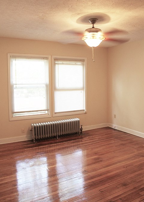 A room with a wooden floor, a ceiling fan, and a radiator.