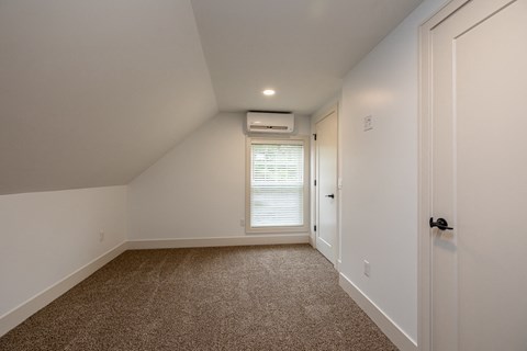 a bedroom with white walls and carpet and a door to a closet