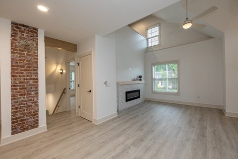 an empty living room with a brick fireplace and wood flooring