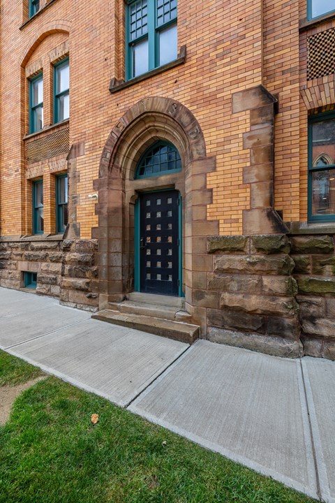 the front of a brick building with a green door and a sidewalk