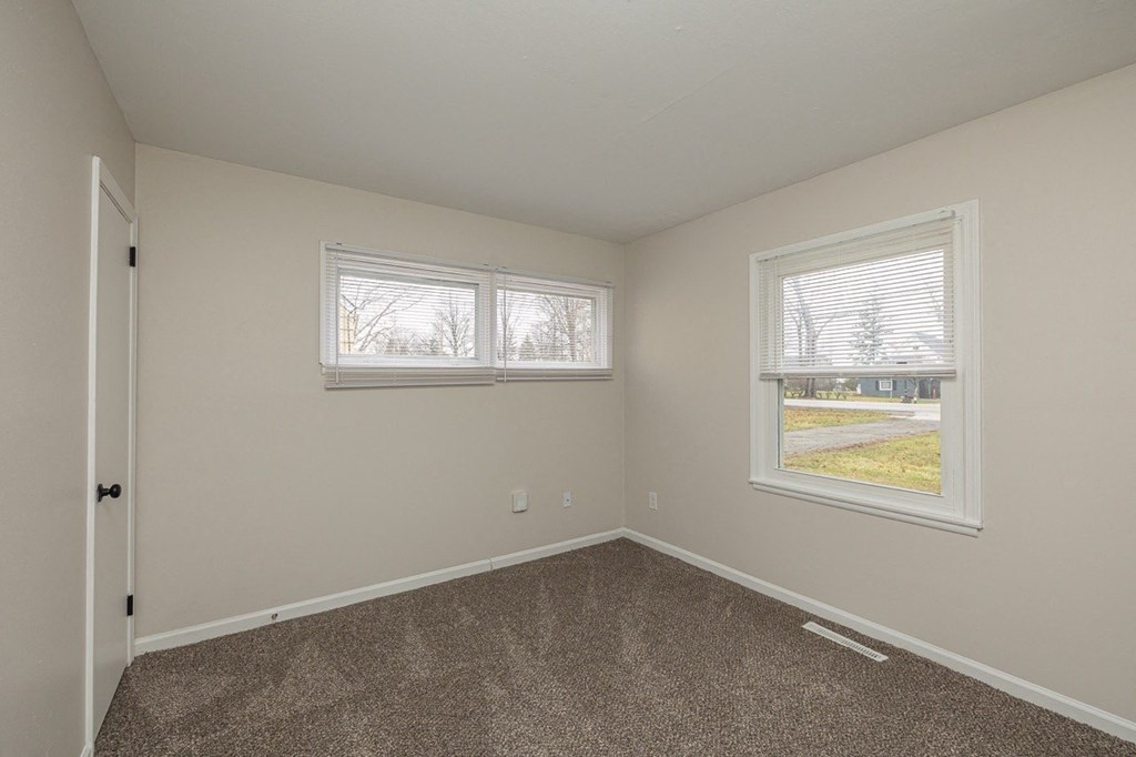 A room with a carpeted floor and two windows.