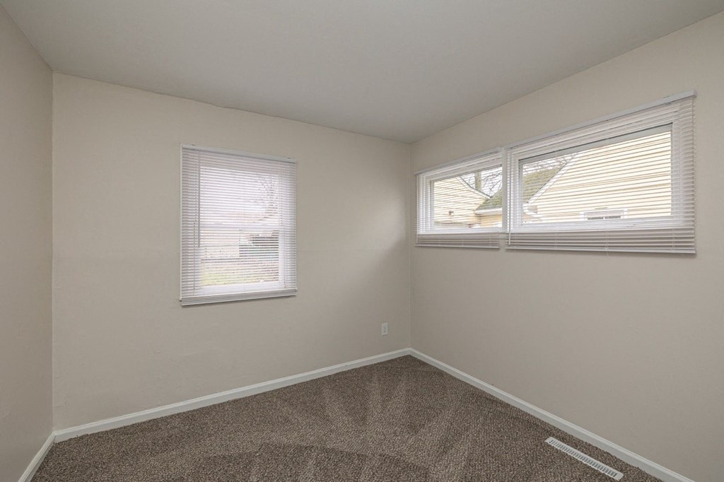 A room with a carpeted floor and two windows.