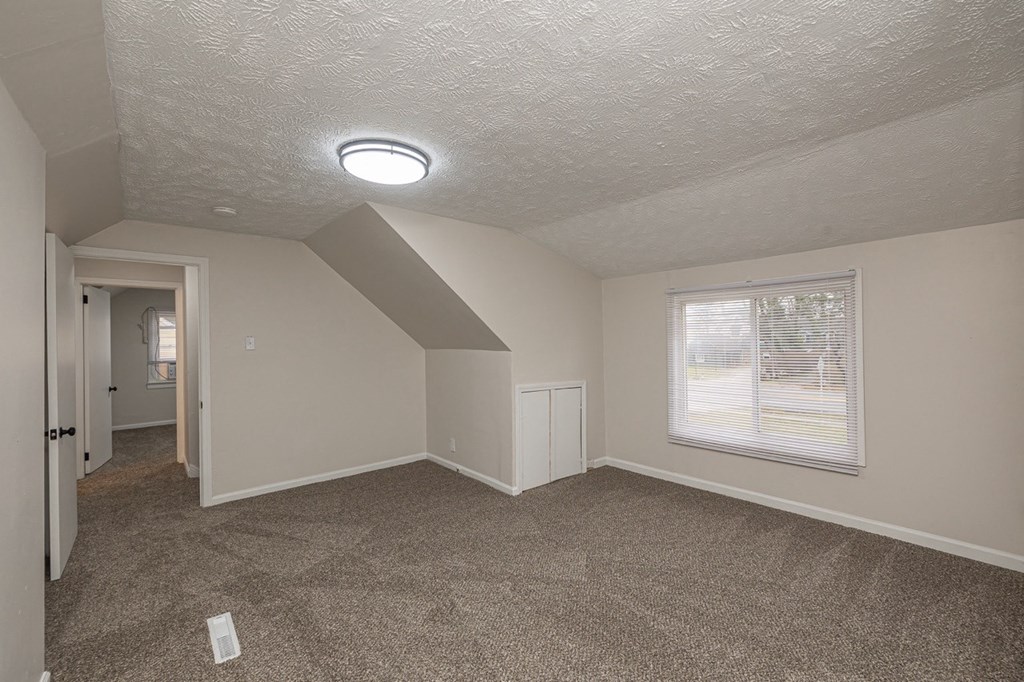 Upstairs bedroom with a newly carpeted floor, storage space, and large window.