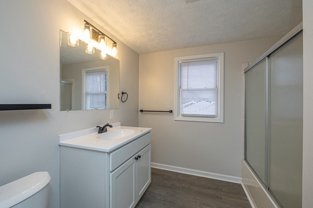 Large bathroom with a glass door tub and white cabinets.