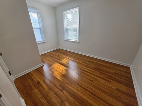 A room with wooden flooring and two windows.