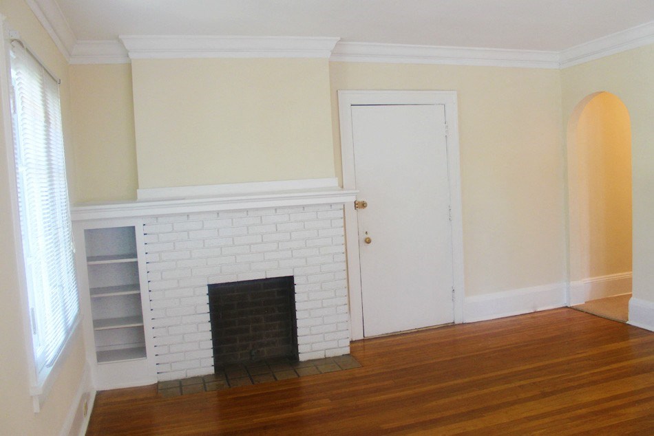 an empty living room with a brick fireplace and wooden floors