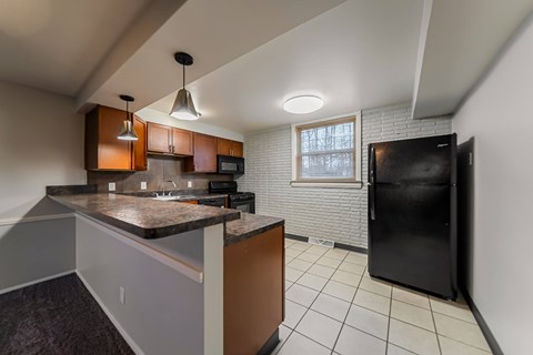 A kitchen with a black refrigerator and brown cabinets.