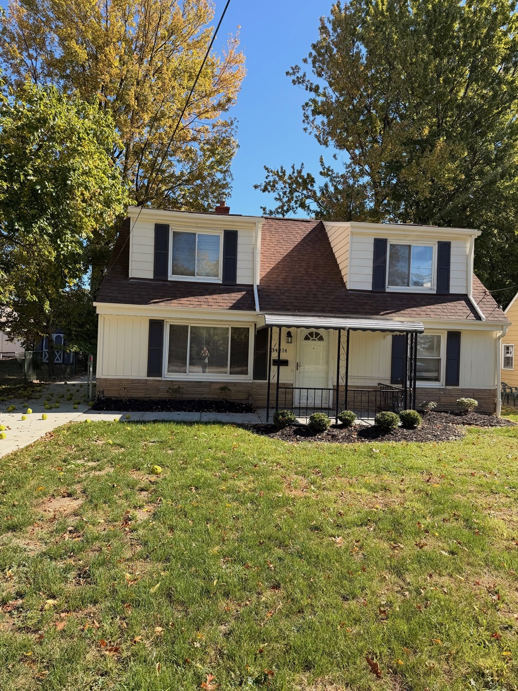 A house with a brown roof and white walls is surrounded by a grassy lawn.