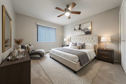A bedroom with a large bed, a ceiling fan, and a nightstand with a lamp.