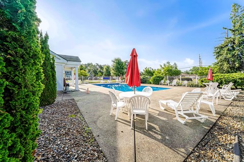 A pool area with chairs and umbrellas is surrounded by a gravel path and greenery.