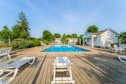 A pool surrounded by white chairs and a wooden deck.