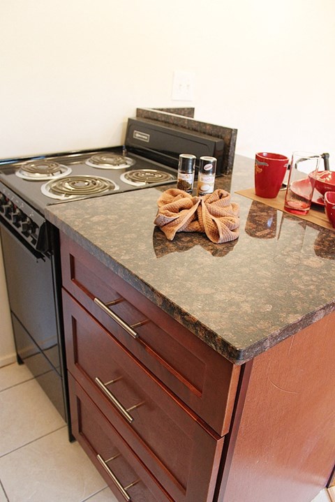 A kitchen counter with a stove top and a red cup on it.