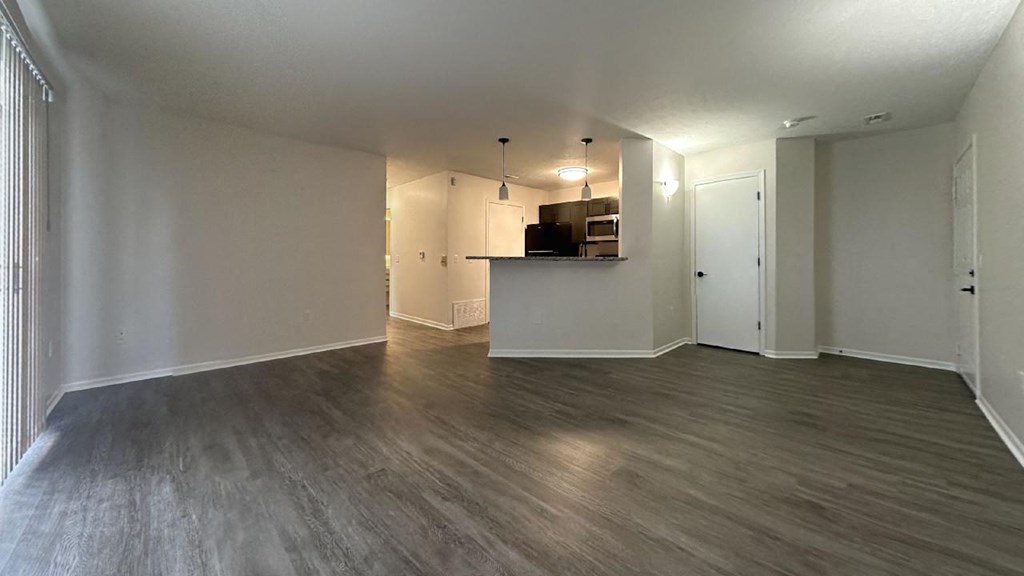 an empty living room with a kitchen in the background