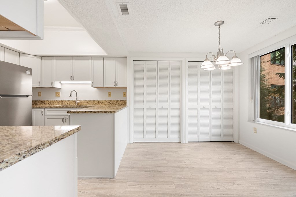 A kitchen with white cabinets and a granite countertop with a dining area.at Atrium in The Village, Beachwood Ohio