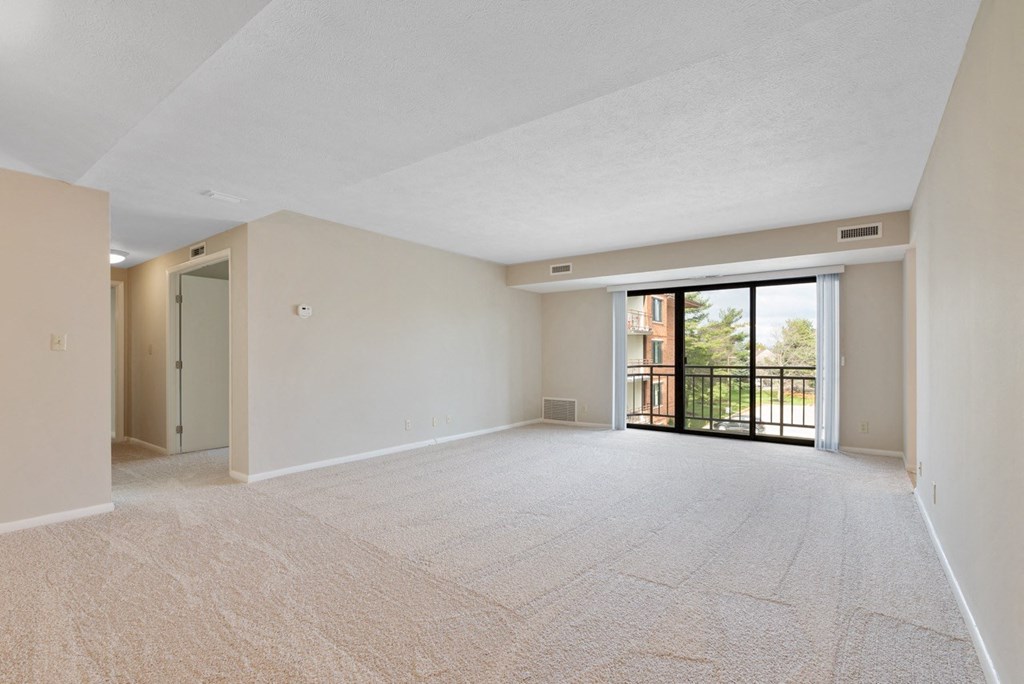 A large living room with a carpeted floor and sliding glass doors leading to a balcony.at Atrium in The Village, Beachwood Ohio