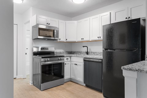 A black refrigerator stands in a kitchen with white cabinets and a black stove.