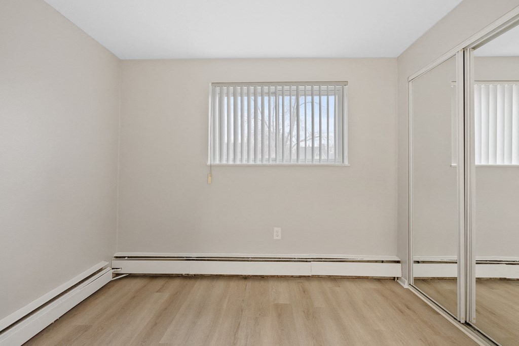 Bedroom with a window, mirrored closet and wooden flooring.
