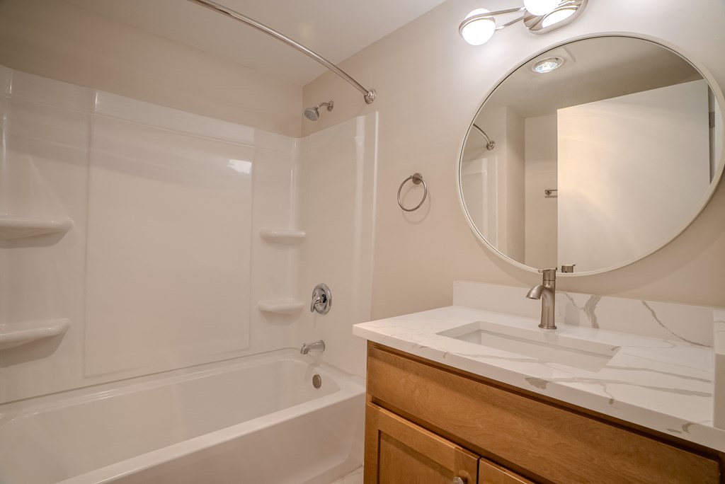 A white bathroom with a round mirror and a white sink t Atrium in The Village, Beachwood