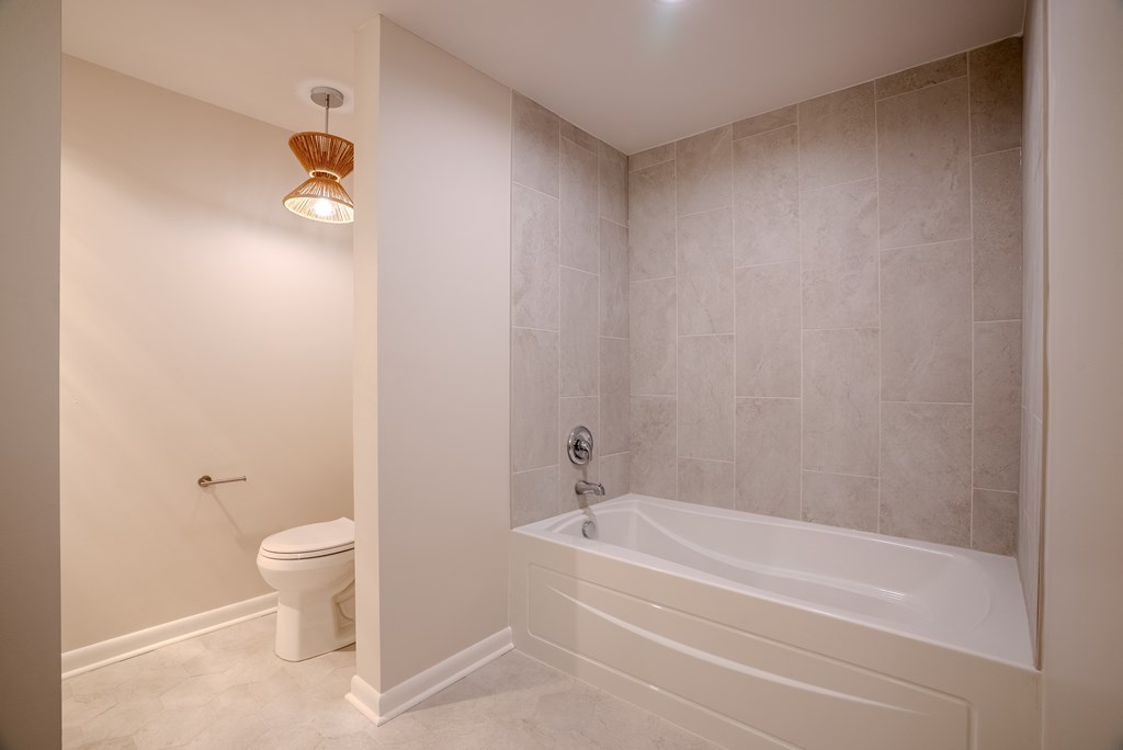 A white bathroom with a toilet, tub, and a light fixture t Atrium in The Village, Beachwood