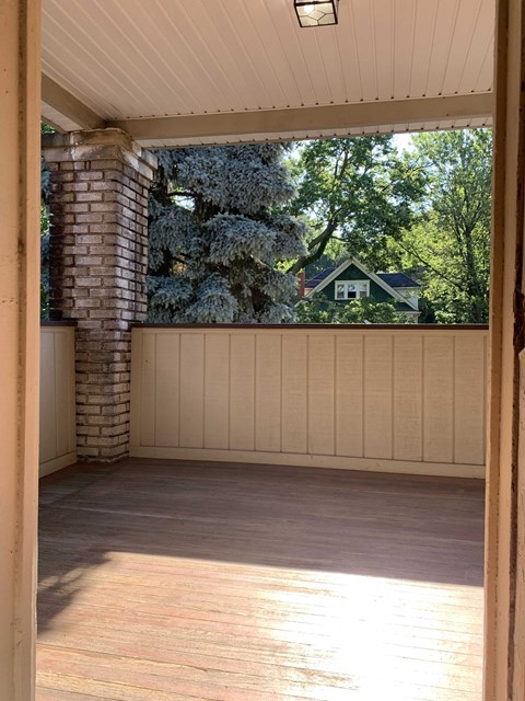 A sunny day in a wooden deck with a view of a green house and trees.