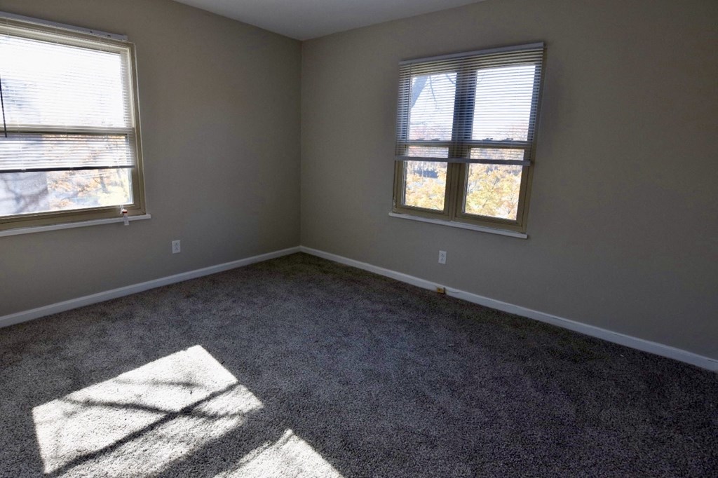 an empty room with two windows and a carpeted floor