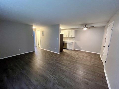 an empty living room with wood floors and a kitchen