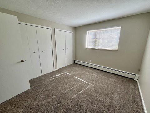an empty room with carpet and a window and closets