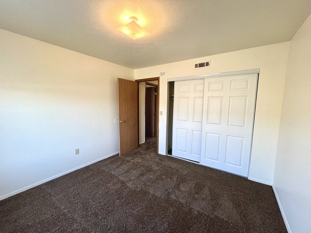 an empty living room with carpet and a door to a bedroom