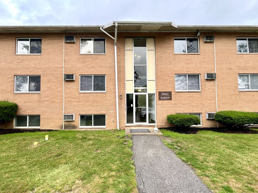 the front of a brick apartment building with a sidewalk and grass